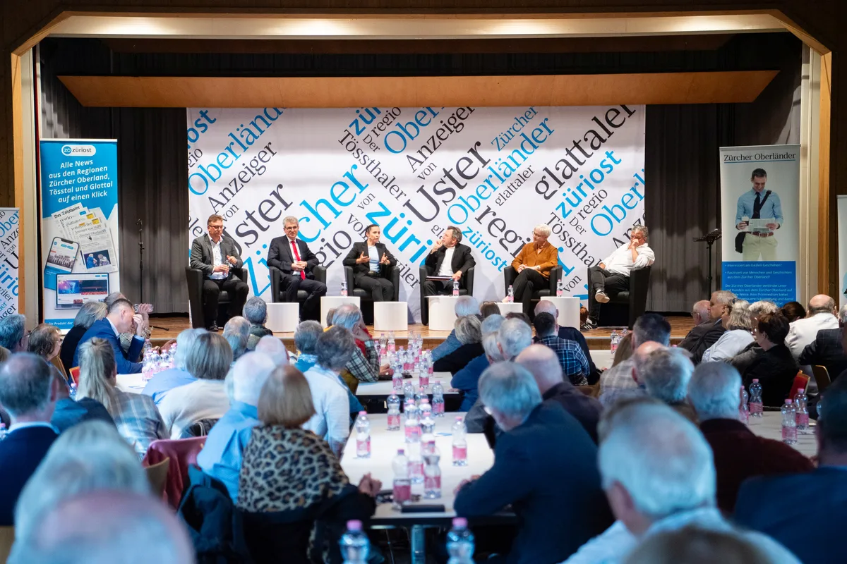Publikum und Podiumsteilnehmende in einem Veranstaltungssaal.